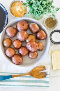 some potatoes are in a white bowl on a table with other ingredients and utensils