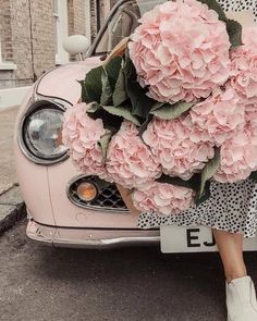 a woman holding a bouquet of pink flowers in front of a car