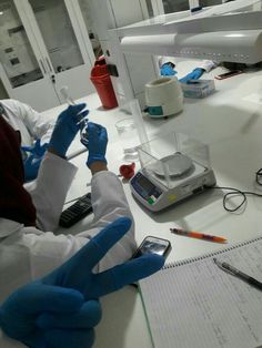 two people in white lab coats and blue gloves working on electronic devices at a table