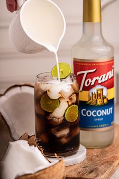 a bottle of torani coconut rum being poured into a glass with ice and limes