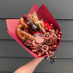 a hand holding a paper bouquet filled with different types of food and drink items in it