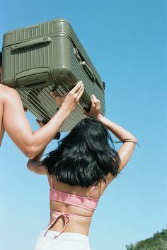 a woman in white shorts carrying a green piece of luggage on top of her head