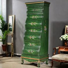 a tall green cabinet with flowers painted on the front and sides, sitting in a living room