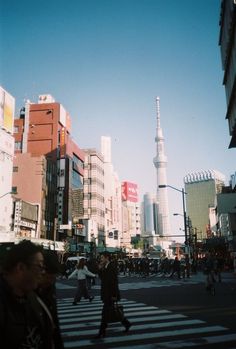 people crossing the street in front of tall buildings and skyscrapers on a sunny day