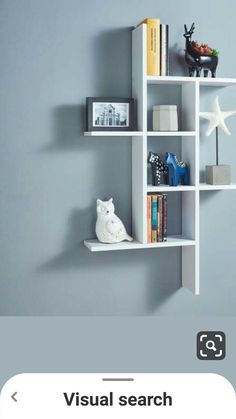 a white shelf with books and other items on it in front of a gray wall