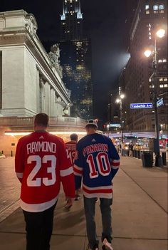 two hockey players are walking down the street at night in new york city, usa