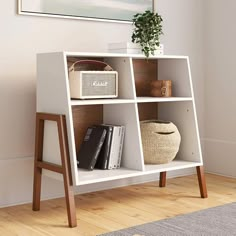 a white book shelf with books and baskets on it in front of a wall mounted painting