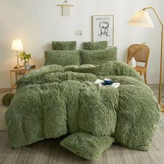 a bed covered in green fluffy comforter next to a table with lamp and chair