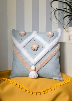 a blue and white pillow with pom poms on it sitting on a yellow chair