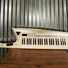 an electronic keyboard sitting on top of a wooden table in front of a metal wall