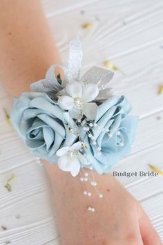 a wrist corsage with blue flowers and silver leaves on the wrist is being held by someone's hand