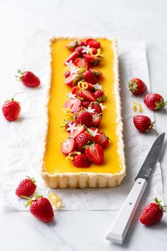 a long pastry with strawberries on it next to a knife and some cut strawberries