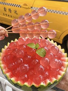 a watermelon fruit bowl with popsicle sticks sticking out of the top and some gummy bears in it