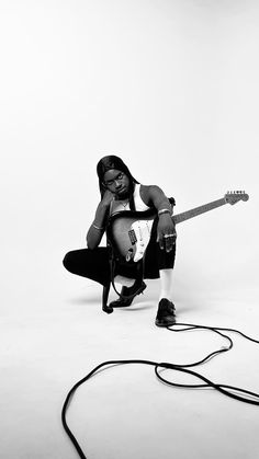 a woman kneeling on the ground with a guitar in her hand and headphones around her neck