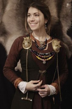 a woman dressed in medieval clothing standing with her hands on her hips and smiling at the camera