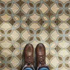 someone wearing brown shoes standing in front of a patterned wall