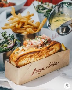 a sandwich in a box with french fries and other food on the table behind it