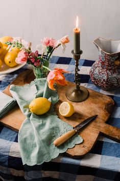 a wooden cutting board topped with lemons next to a vase filled with flowers and a knife