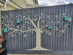 a tree painted on the side of a wooden fence with bird houses attached to it