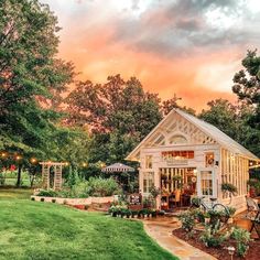 a small white house sitting in the middle of a lush green field with trees around it