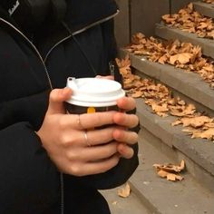 a woman holding a cup of coffee in her hand while standing next to some stairs