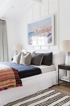 a bedroom with white walls, black and white bedding, striped rugs and pictures on the wall