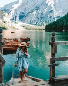 a woman in a blue dress and hat standing on a dock next to some boats