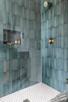 a blue tiled shower with gold fixtures and white hexagonal tiles on the walls