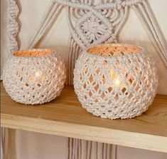 two white crocheted candle holders sitting on top of a wooden shelf next to a macrame wall hanging