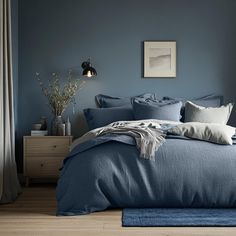 a bed with blue sheets and pillows in a room next to a lamp, dresser and window