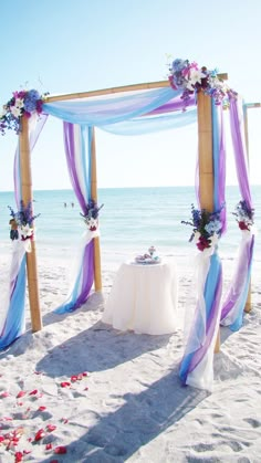 an outdoor wedding setup on the beach with blue and purple draping over it