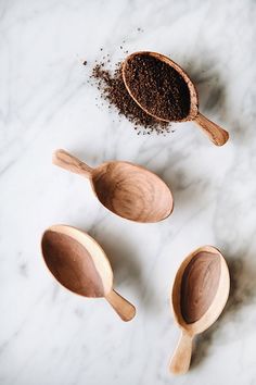 three wooden spoons filled with ground coffee on top of a white marble countertop