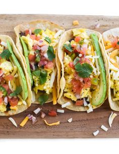 three breakfast tacos are lined up on a cutting board