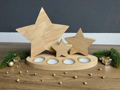 three wooden stars on a stand with christmas decorations around the base and behind it is a candle holder