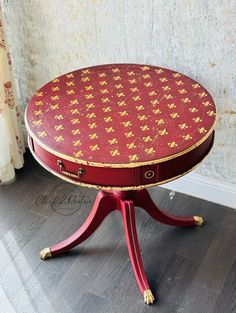 a small red table with gold designs on it's top and legs, sitting in front of a wall