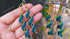 two pairs of gold and blue beaded earrings hanging from a tree branch in front of a hand