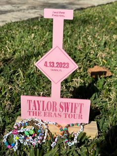 a pink sign sitting on top of a lush green field next to a wooden post