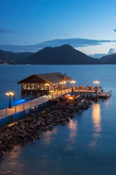 a dock that has some lights on it near the water and mountains in the background