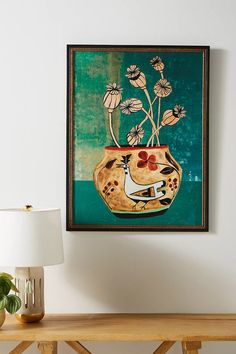 a painting hanging on the wall next to a table with a lamp and potted plant