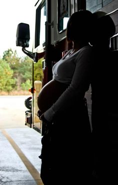 a pregnant woman standing in front of a fire truck with her hand on the door