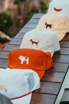 three hats sitting on top of a wooden table next to each other and one has a dog embroidered on it