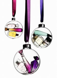 three glass ornaments with different types of perfumes in them hanging from purple ribbon on white background