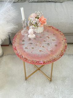 a pink table with flowers on it in front of a gray couch and white fur