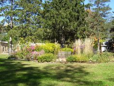 a park bench sitting in the middle of a lush green field next to flowers and trees