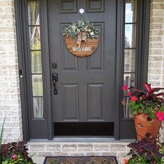 a welcome sign on the front door of a house with potted plants and flowers