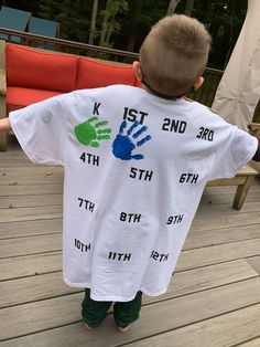 a young boy wearing a white shirt with blue and green handprints on it