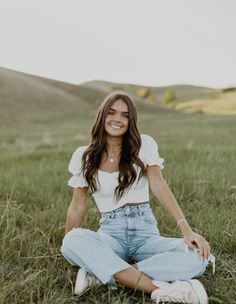 a woman sitting in the grass with her hands on her hips and smiling at the camera