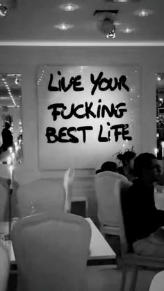 black and white photograph of people sitting at tables in a restaurant with writing on the wall