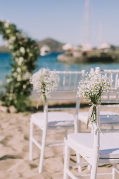 white chairs with baby's breath flowers tied to them on the sand at a beach