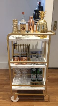 a gold bar cart filled with liquor bottles and glasses on top of a hard wood floor